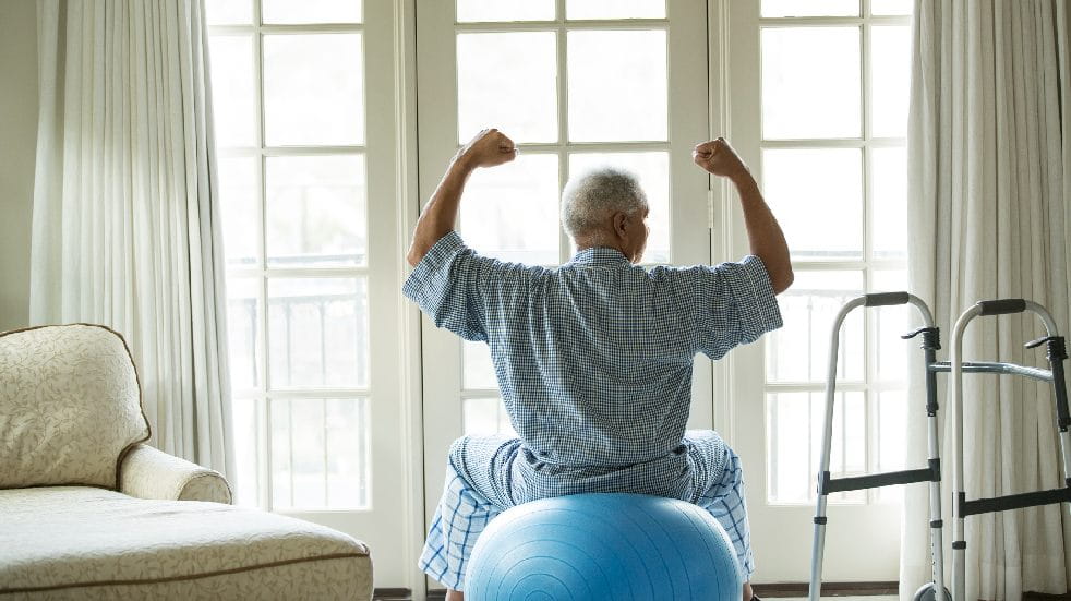 older man sitting on exercise ball next to a walker